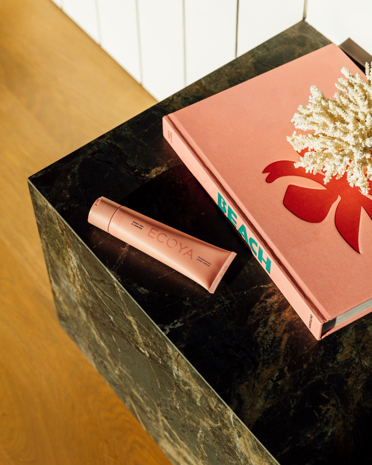 Coral Ecoya hand cream on a timber table beside a pink book