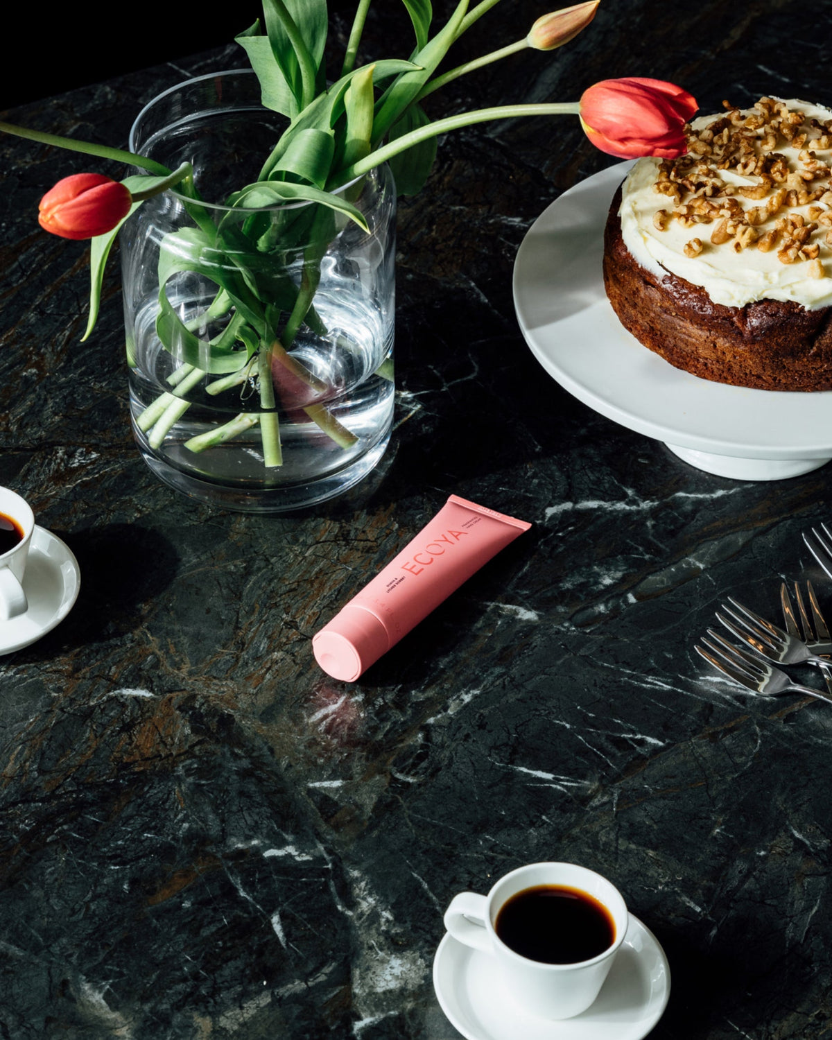 Coral Ecoya hand cream tube on green marble beside tulips, coffee and cake