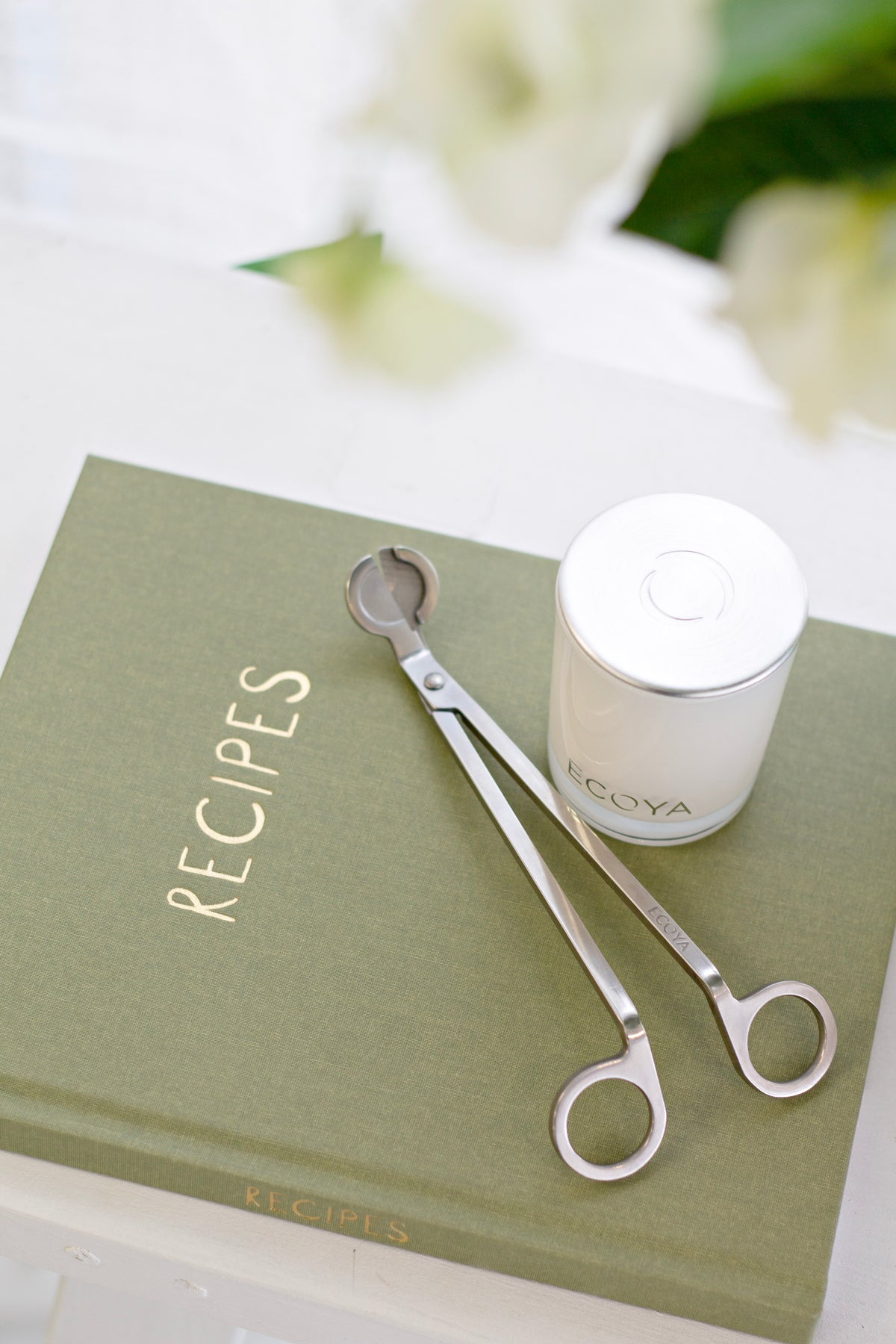 Olive Write To Me recipe journal with a white candle and silver wick trimmer on a white table