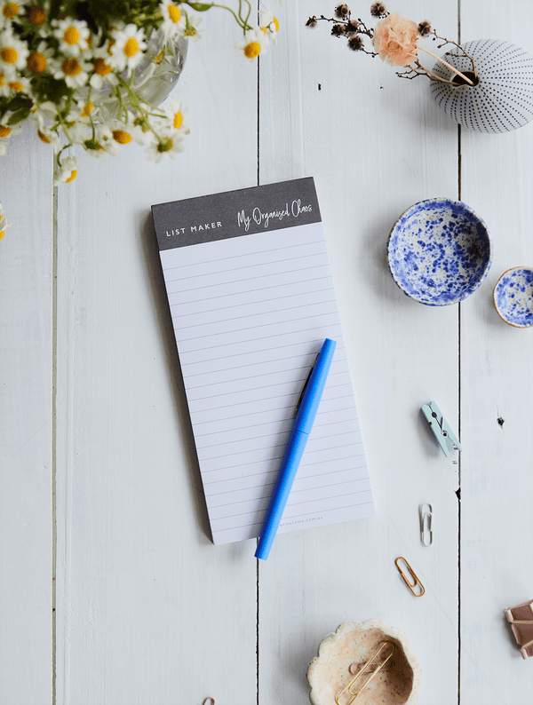 A LIST MAKER list pad with a blue pen on a wooden table. (Brand Name: Write To Me)