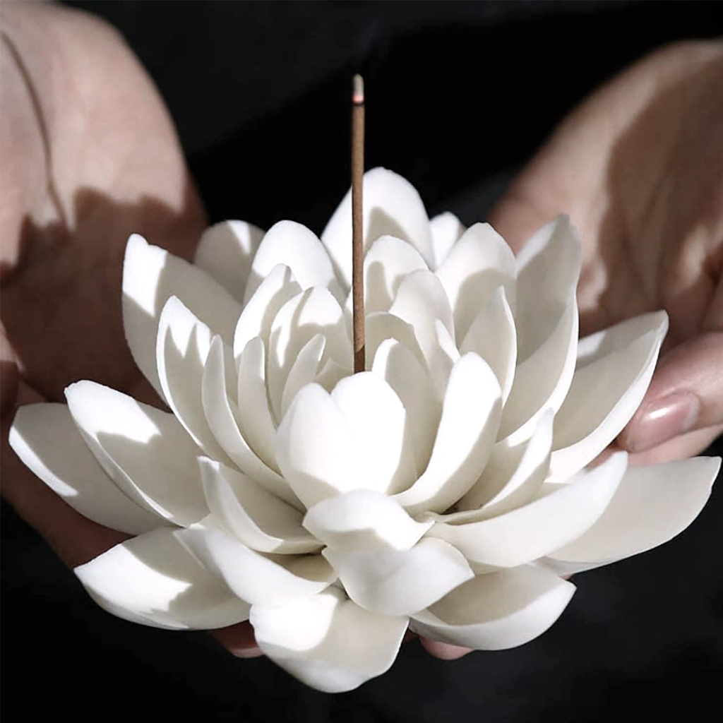 Hands cradling the white lotus incense holder with a lit stick rising from its centre
