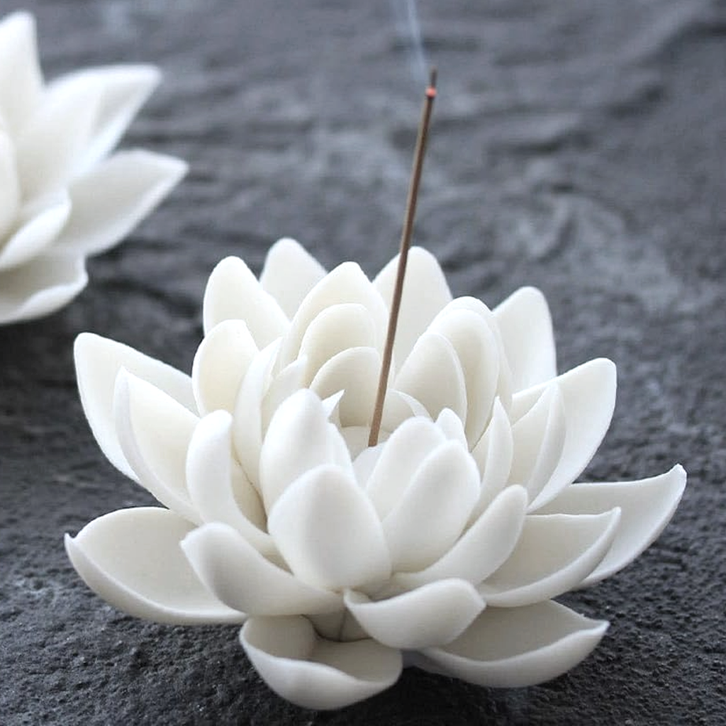 Lotus incense holder on dark stone with a stick burning in the centre and a second holder behind