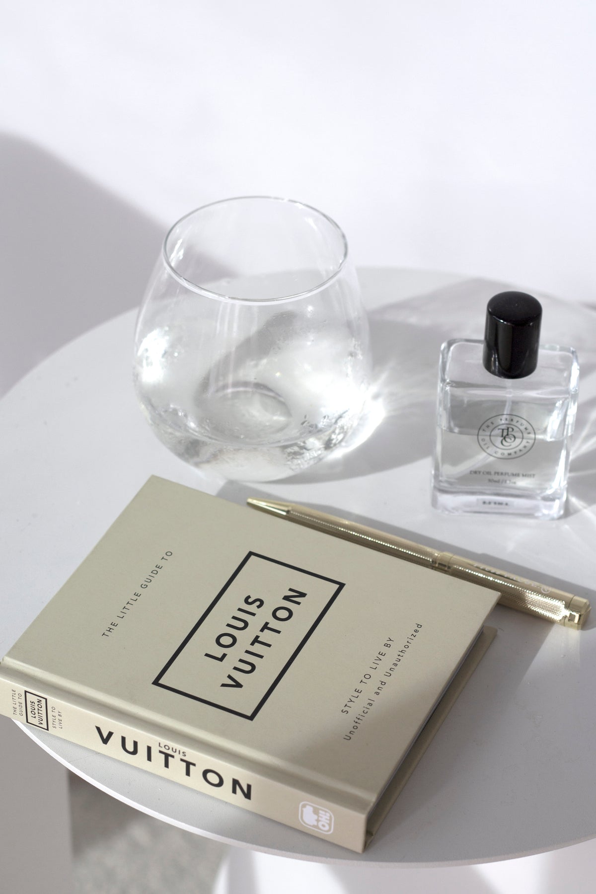 Louis Vuitton Little Book on white side table with gold pen, glass, and perfume – chic fashion coffee table styling.