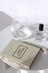 Louis Vuitton Little Book on white side table with gold pen, glass, and perfume – chic fashion coffee table styling.