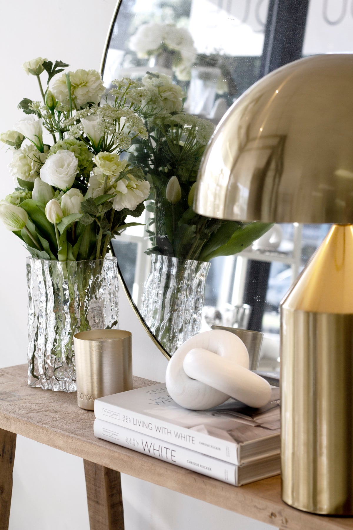 Brass dome lamp beside white blooms in textured glass vases, with an arched mirror behind