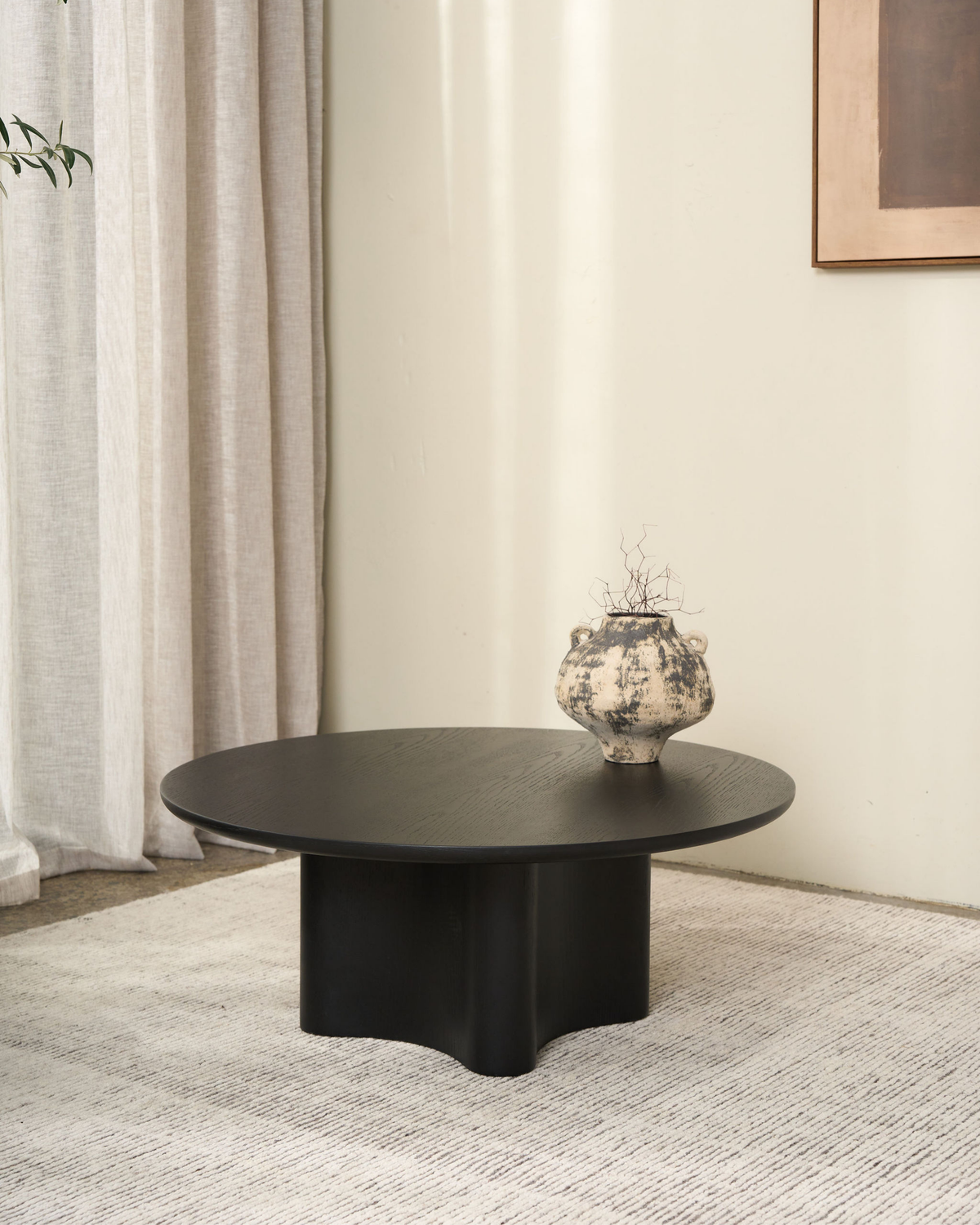 Black Oak Luma Coffee Table with a mottled cream and charcoal handled vase holding dried twigs