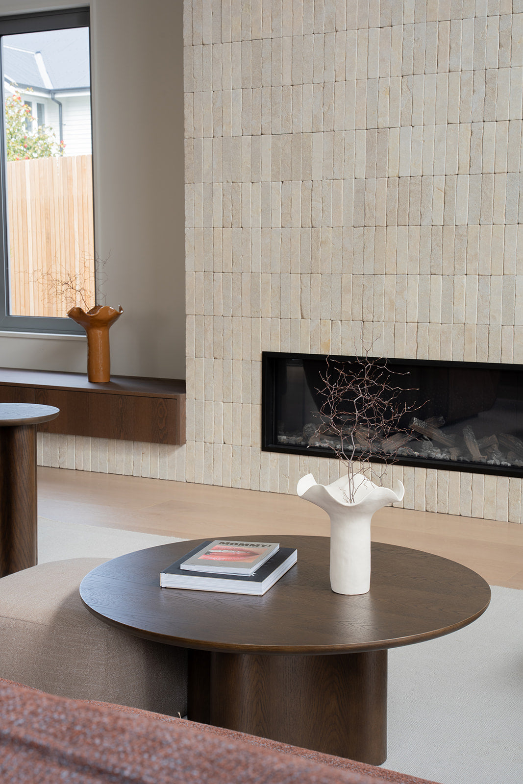 Brown Oak Luma Coffee Table with books and a white ruffled vase near a fireplace and window seat