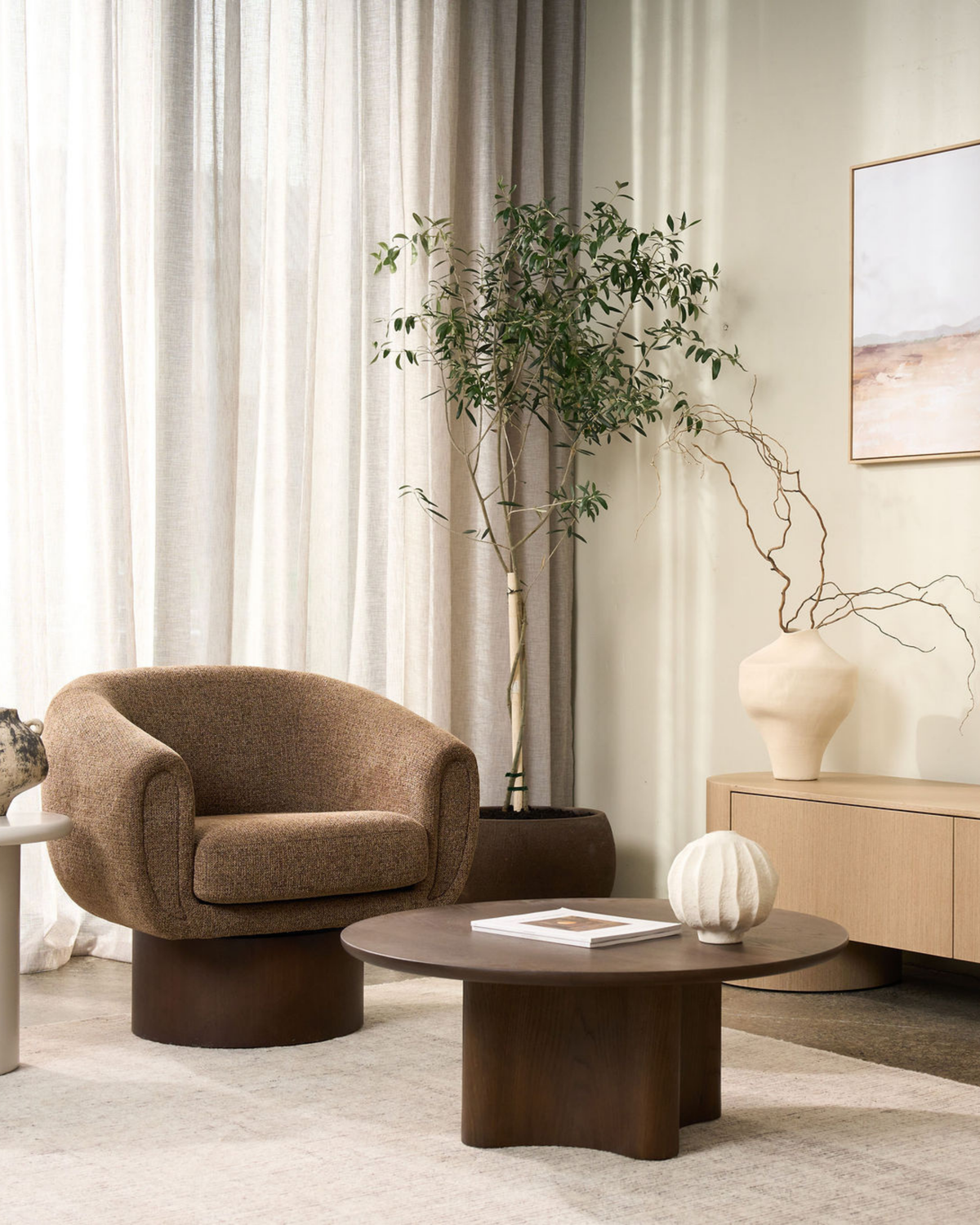 Brown Oak Luma Coffee Table in front of a brown boucle swivel armchair and a potted olive tree