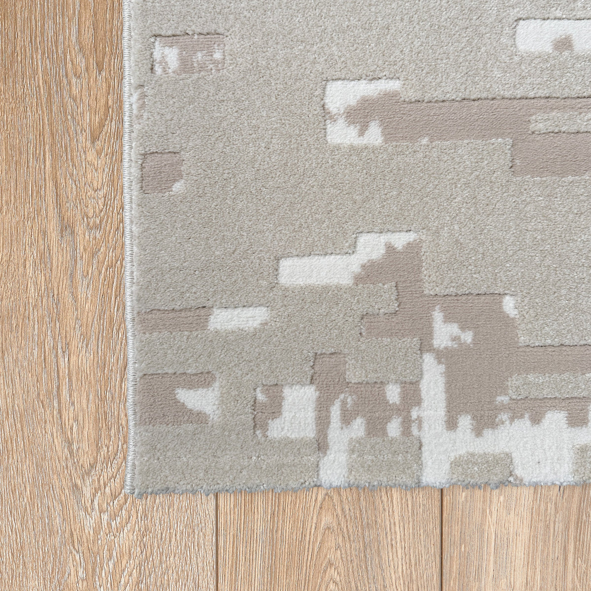 Corner of the beige and ivory abstract rug on a light timber floor