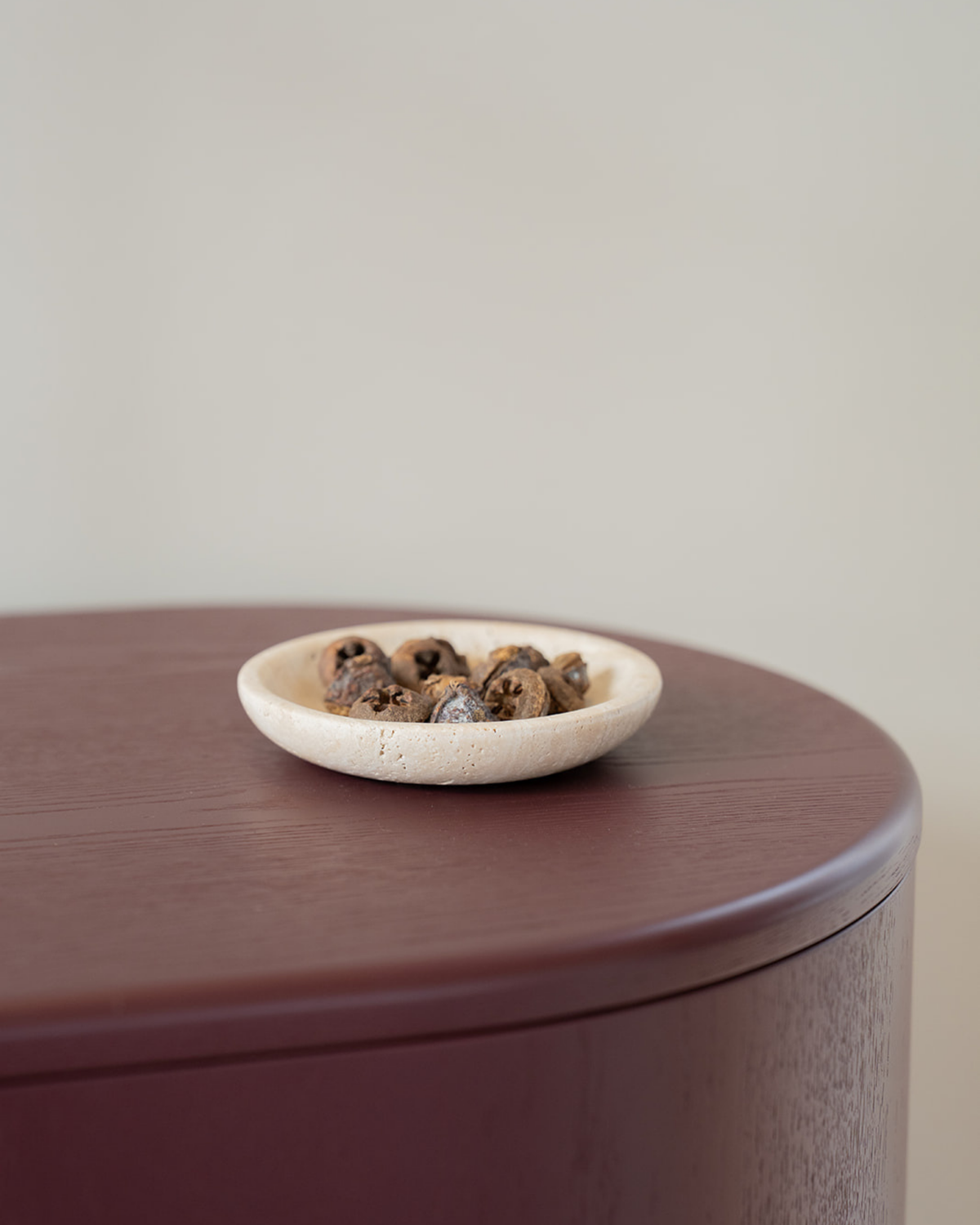 Light Travertine bowl holding dried fruit on the curved edge of a burgundy timber cabinet
