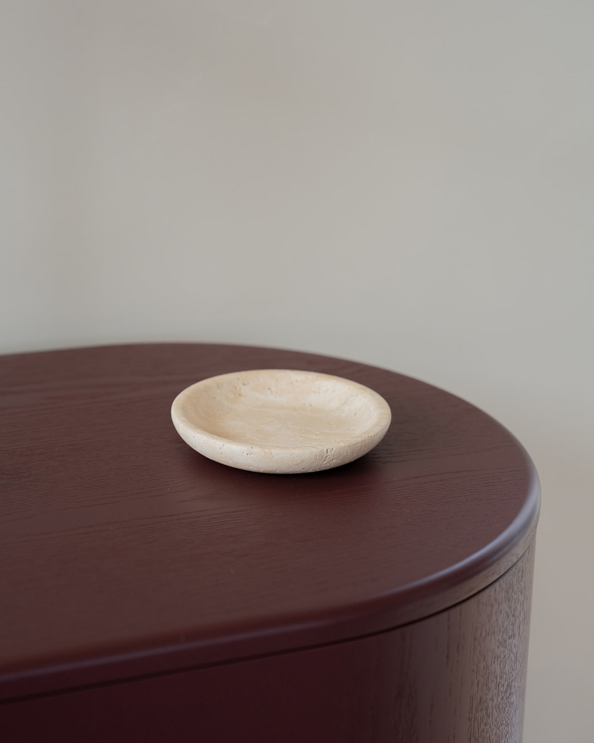 Empty Light Travertine Luvi Bowl on a burgundy timber surface, showing its rounded rim