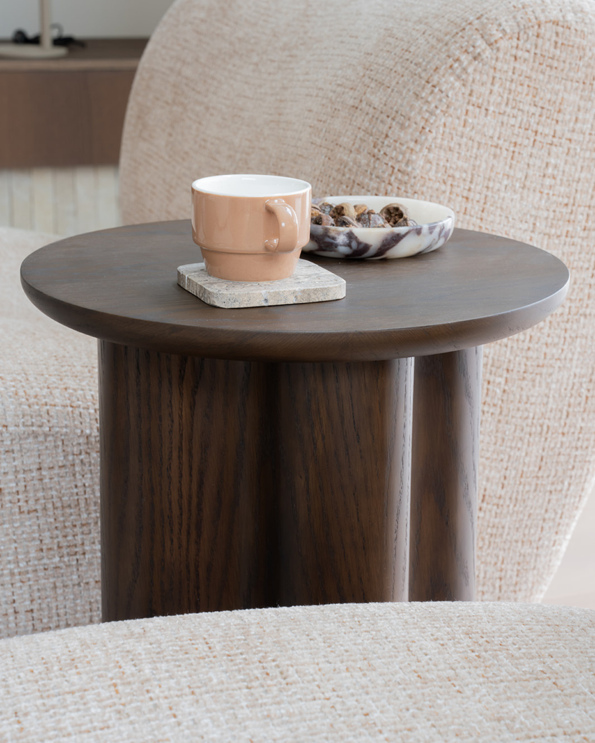 Viola Marble bowl of dried fruit beside a tan mug on a stone coaster, on a timber table by a boucle chair