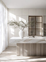 Lyra white sculptural stone-textured vase with wide olive branch arrangement on marble and timber kitchen island with floor-to-ceiling sheer curtains