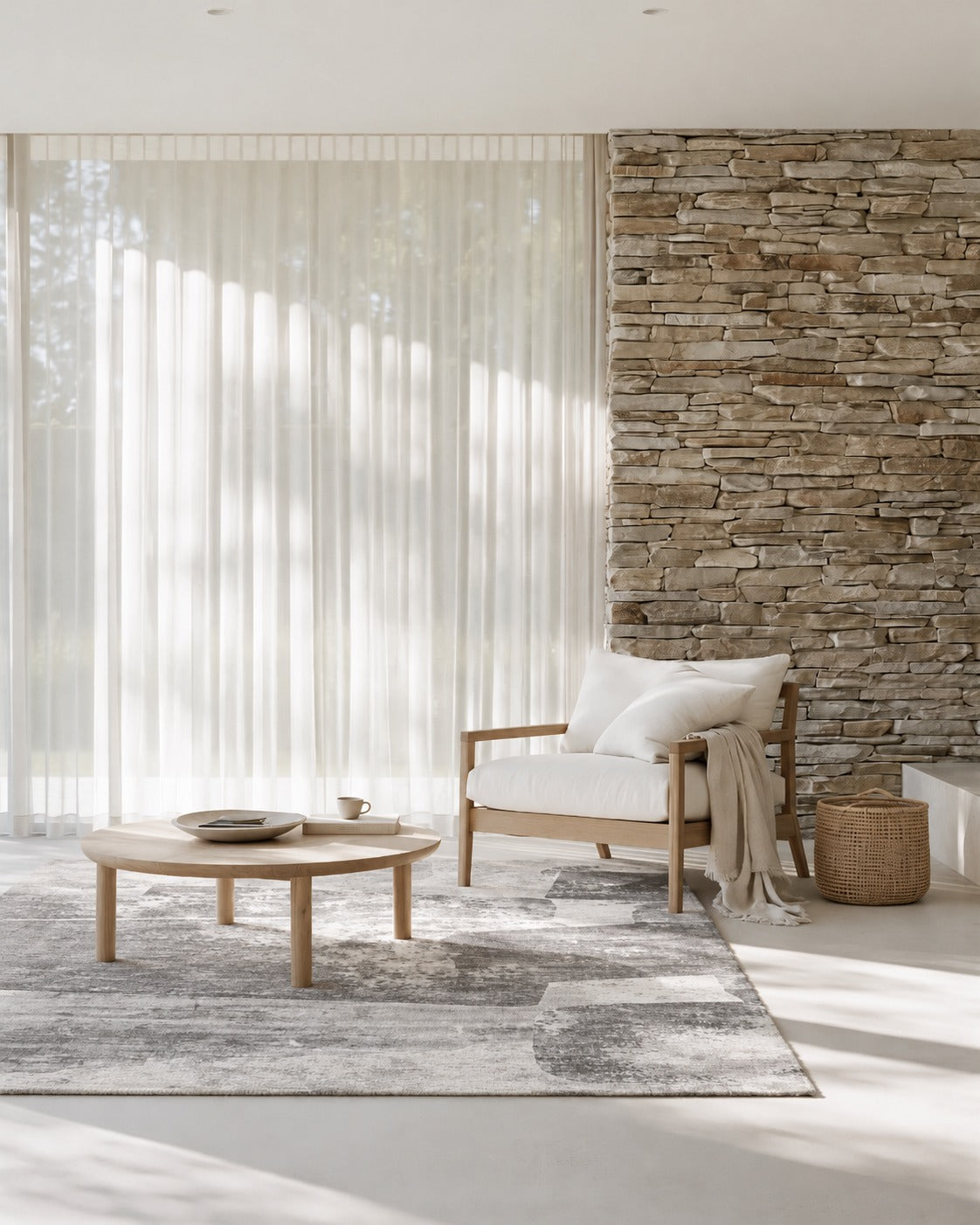 Malta Shadow Rug under a round timber side table and a cream armchair beside sheer curtains and a stacked stone wall