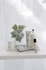 Marble look silicone tray styling set with soap, hand cream, bottle and glass vase on a white bench
