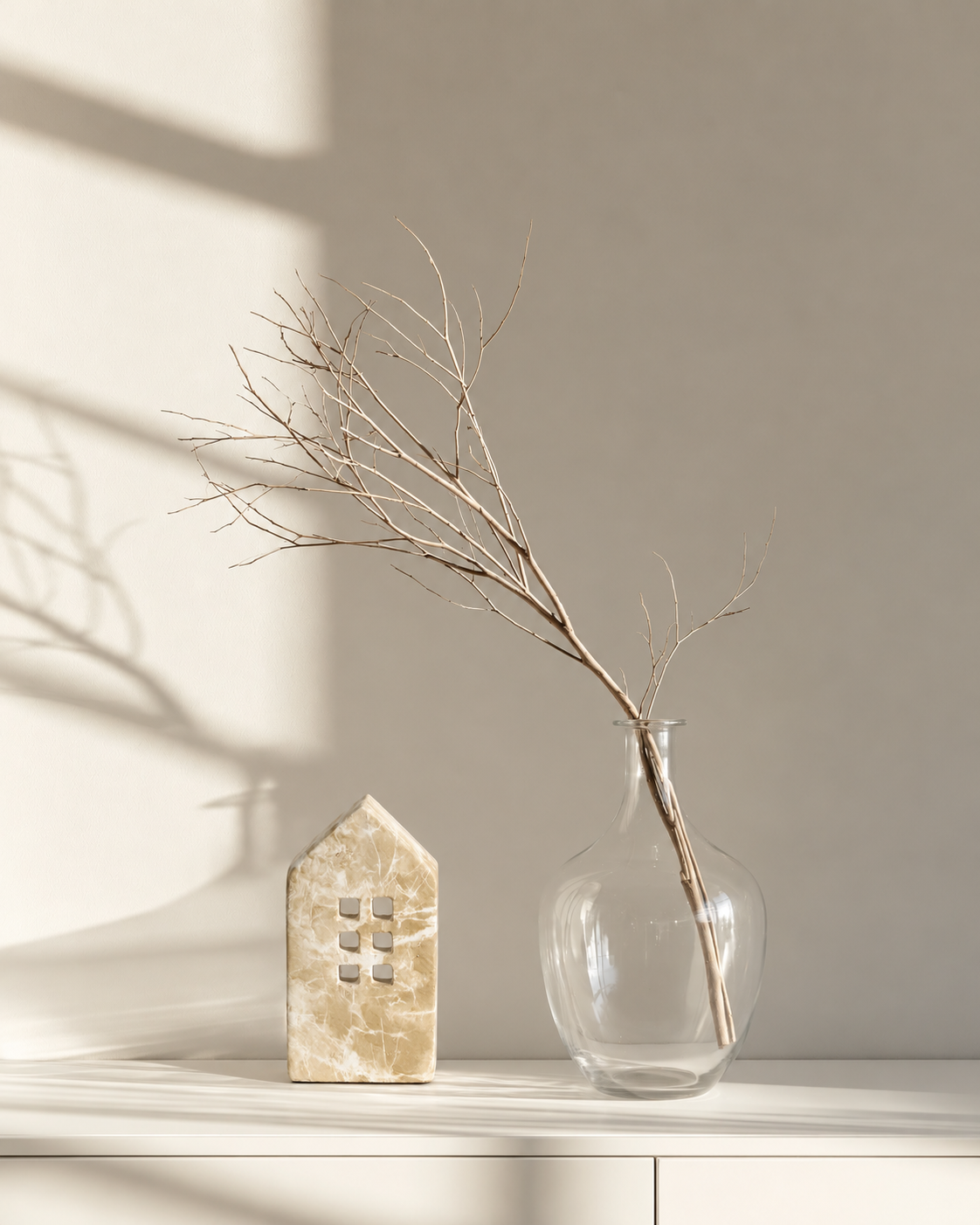 Marble-look townhouse on a white sideboard beside a glass vase with a bare branch in soft window light