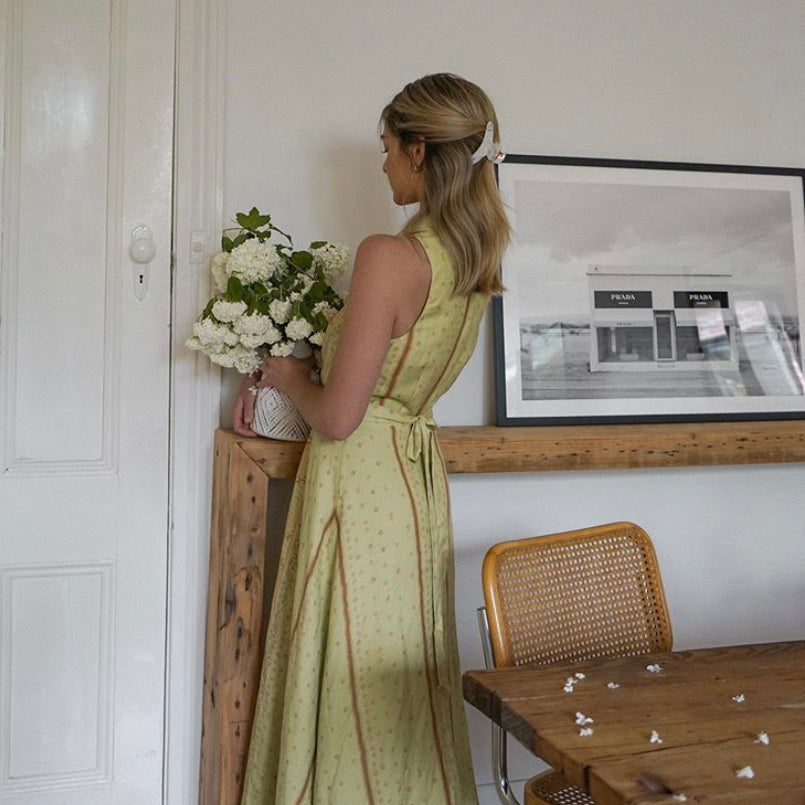 Woman arranging flowers beneath the Marfa print in a black frame on a timber shelf