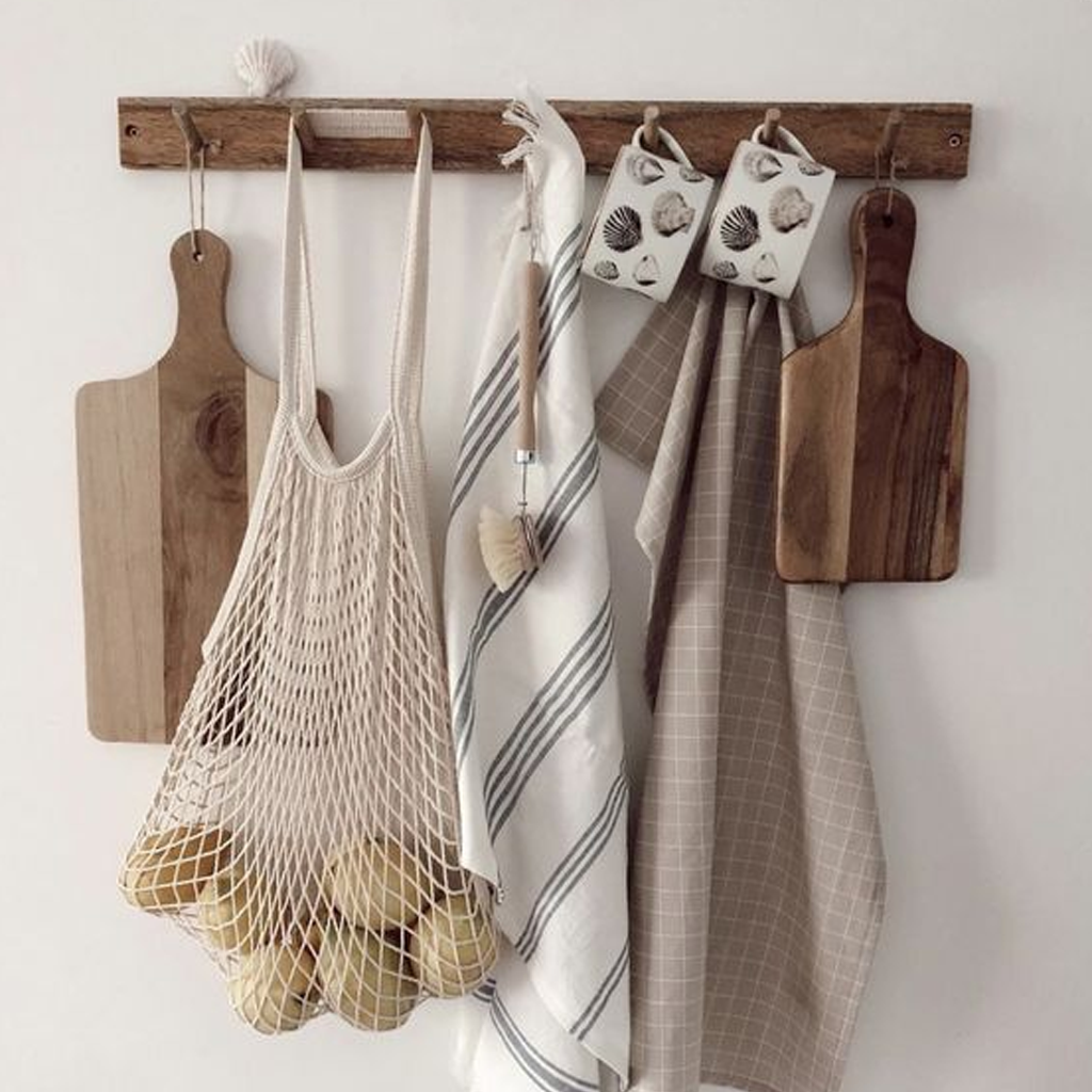 Cream string bag on a peg rail beside wooden chopping boards and striped tea towels
