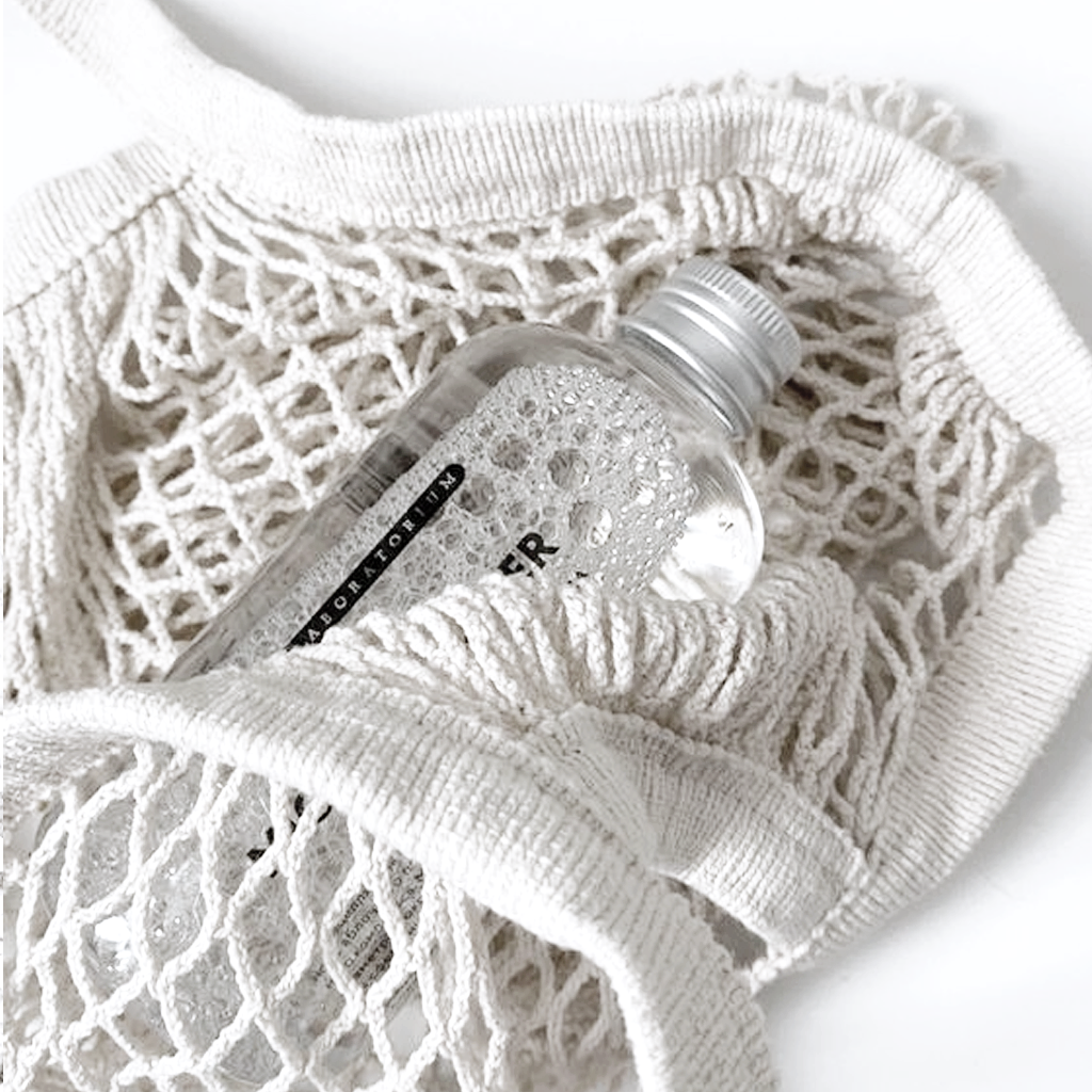 Clear glass bottle resting inside the cream string bag, showing the open weave up close