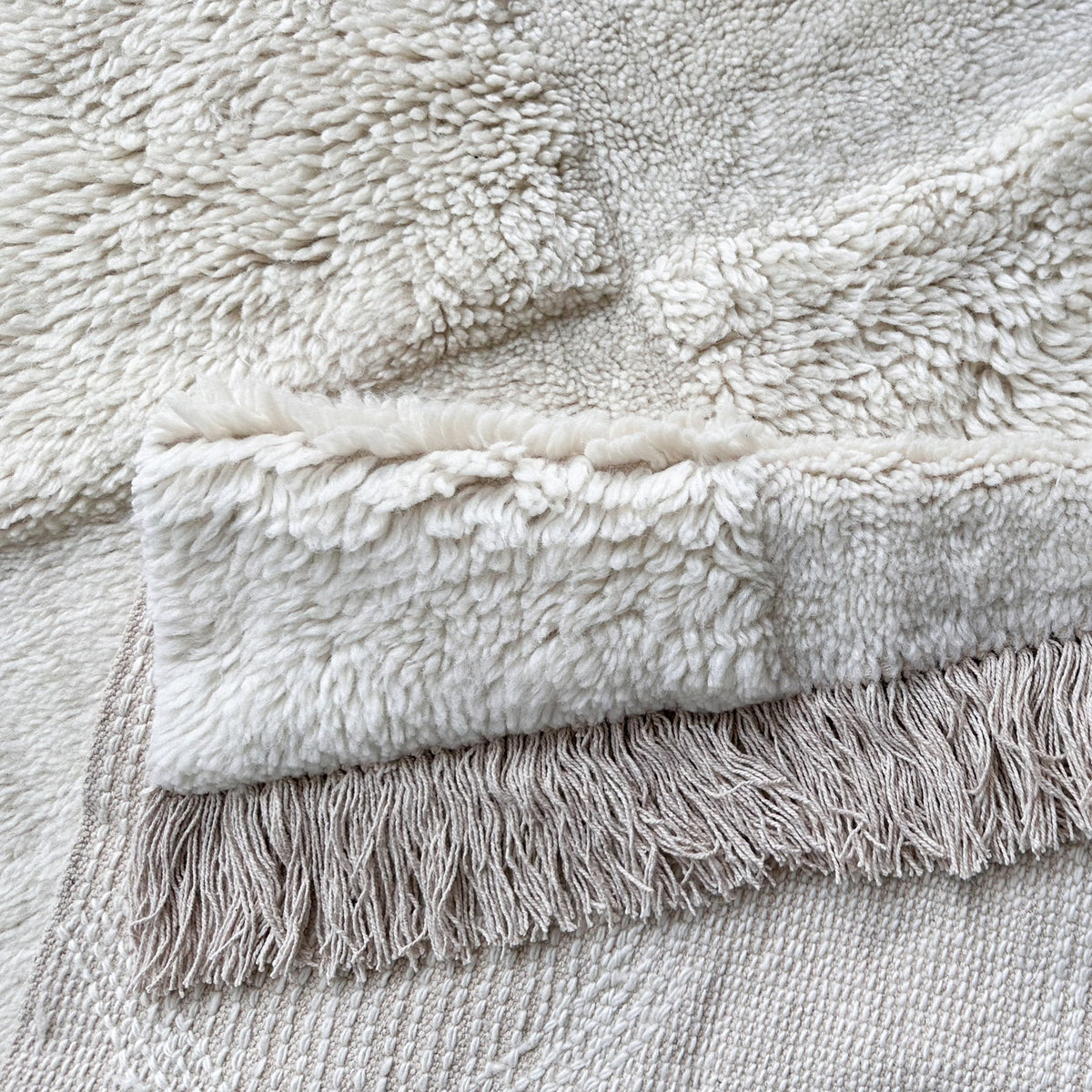 Ivory wool rug folded over to show the fringed end and woven backing