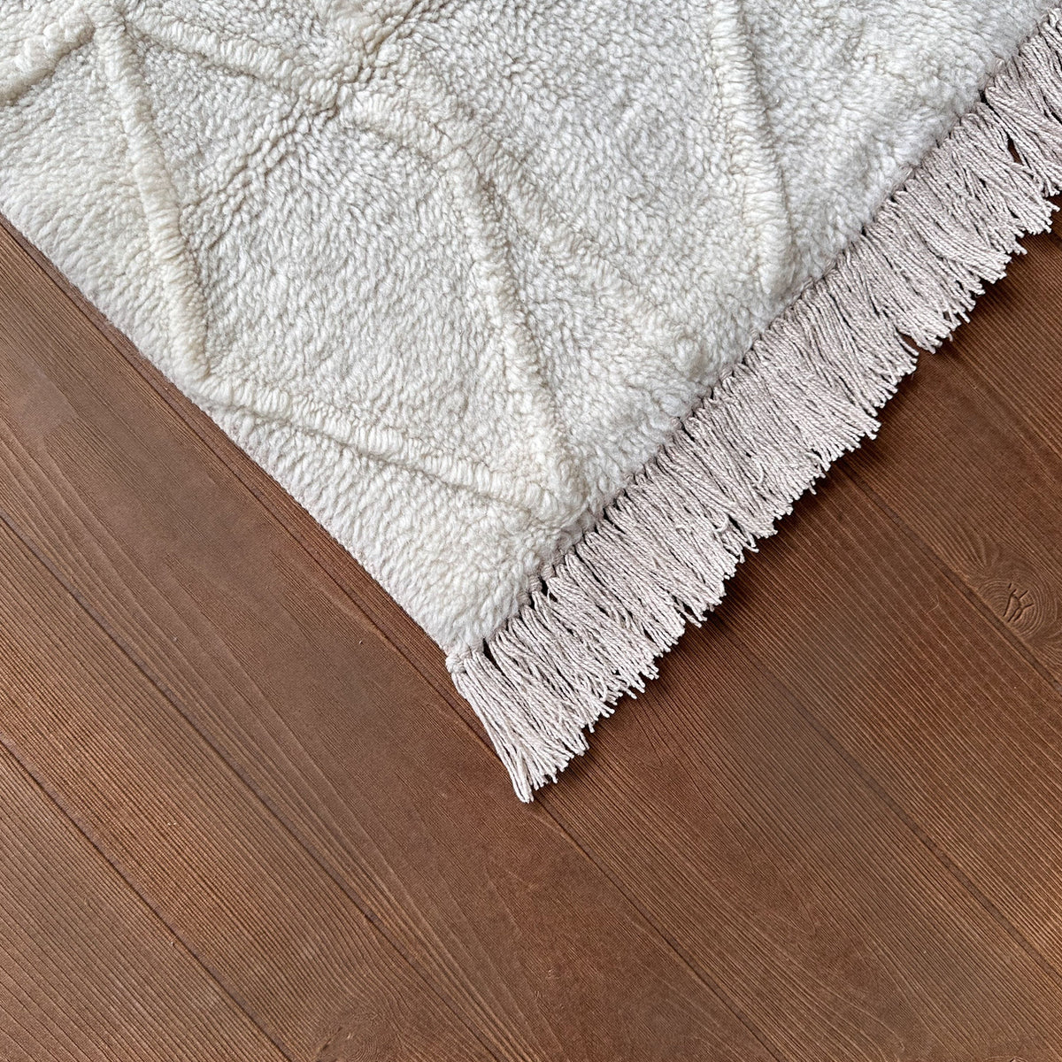 Corner of the ivory wool rug with its fringe on a dark timber floor