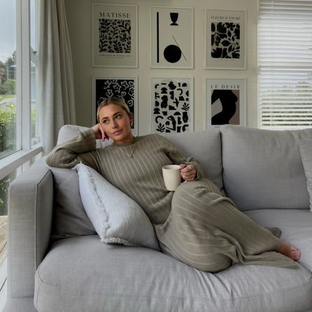 Woman with a mug on a grey sofa beneath a gallery wall featuring the Matisse print
