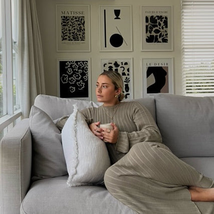 Woman relaxing on a grey sofa beneath a gallery wall featuring the Matisse print