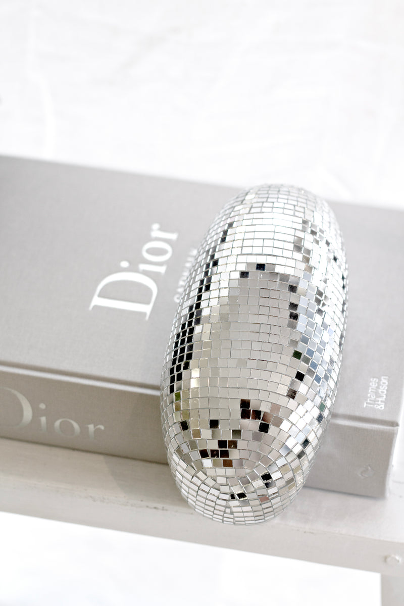 Melting disco ball sculpture with mirrored mosaic tiles styled on a Dior coffee table book for modern reflective decor.
