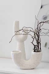 Mia off-white speckled pipe vase styled with sculptural branches beside a curved mirror on a white console.