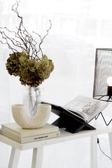 Speckled off-white cement pipe vase with double openings styled on books, modern sculptural décor piece for minimalist interiors