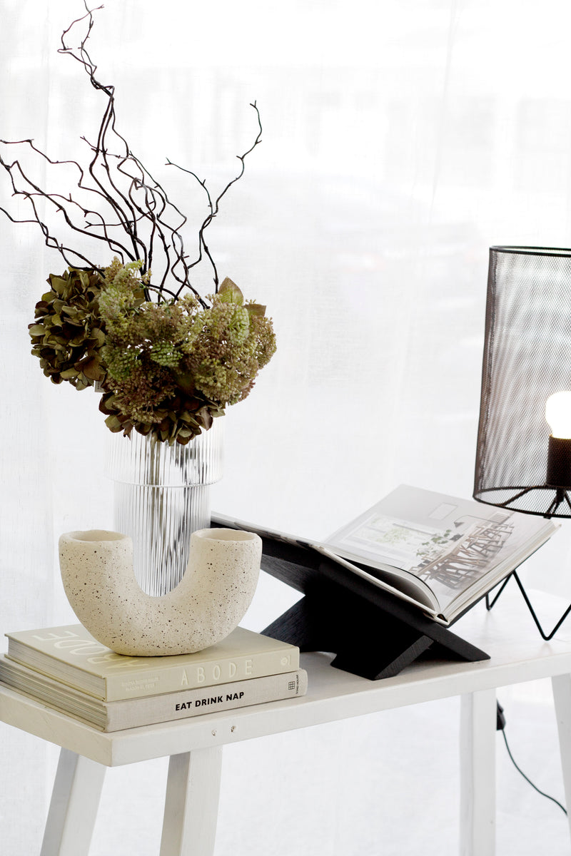 Speckled off-white cement pipe vase with double openings styled on books, modern sculptural décor piece for minimalist interiors