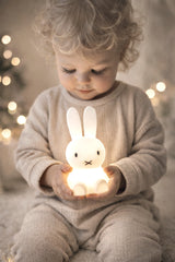Toddler holding glowing Miffy Bundle of Light night lamp in soft neutral nursery setting