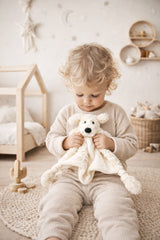 Toddler holding Milo the Puppy comforter in neutral minimalist nursery