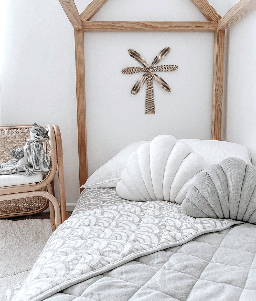 Small Shell Cushion in Mist with a larger ivory shell cushion on a kids bed beneath a palm wall hanging