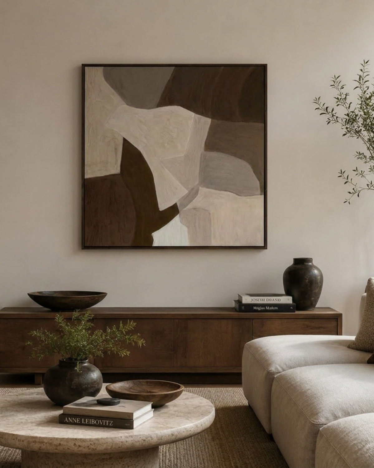 Mood Print above a walnut sideboard with a dark bowl, black vase, books, travertine coffee table and cream sofa