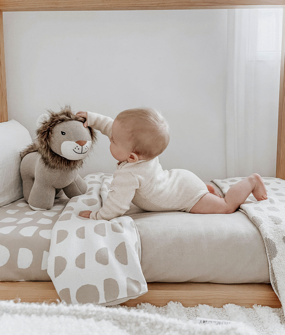 Baby with a knitted lion toy on a floor bed dressed in a Moon Phase fitted sheet and matching duvet cover