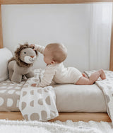 Baby on a neutral bed with moon phase jersey cotton sheets, knitted lion toy and soft oatmeal nursery styling