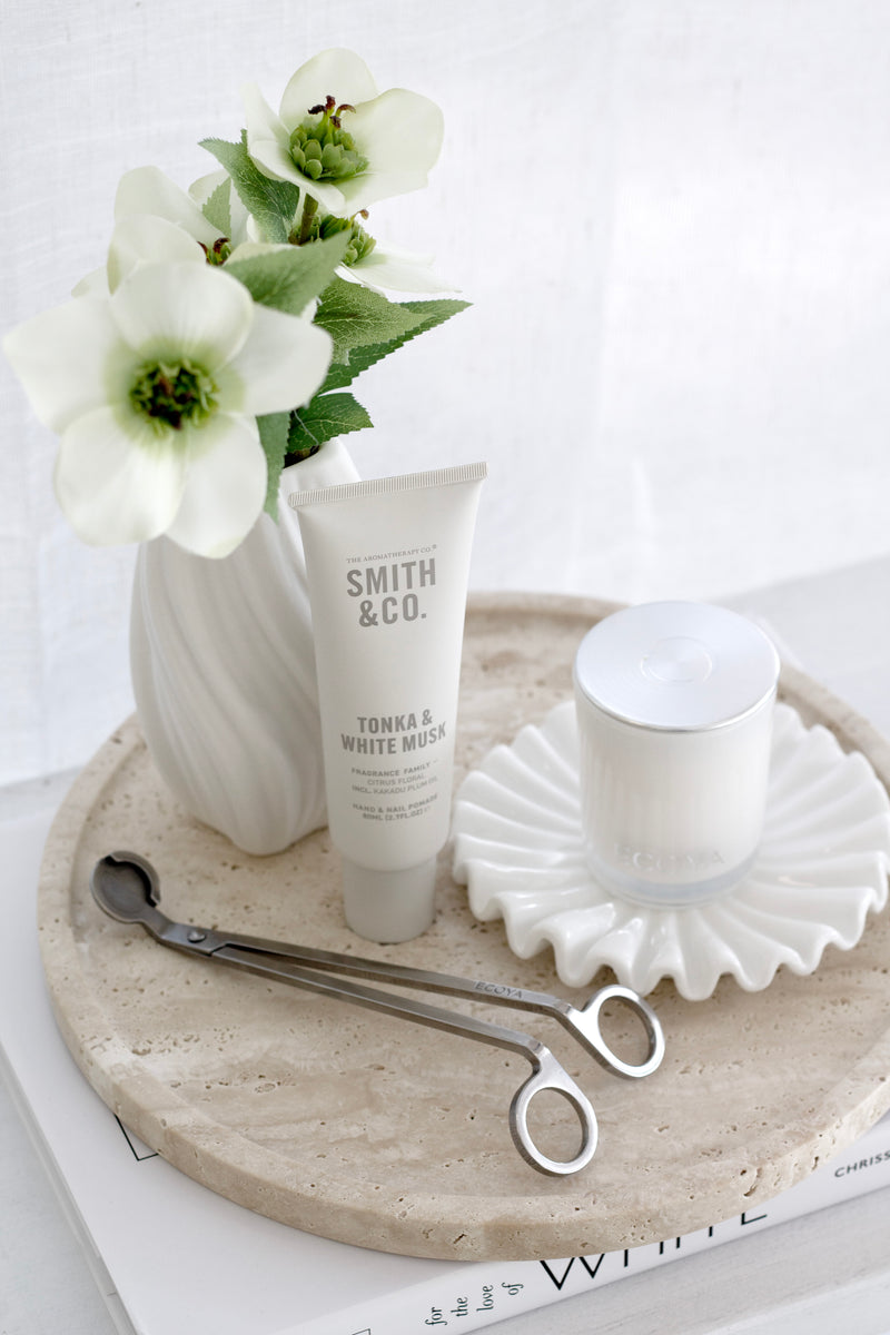 Round travertine tray styled with candle, hand cream, and vase for elegant bathroom or coffee table decor