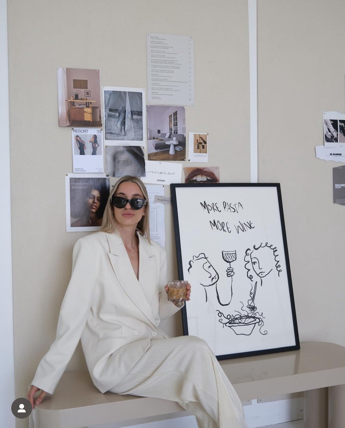 Woman in a white suit sitting beside the More Pasta More Wine print with a pinboard behind