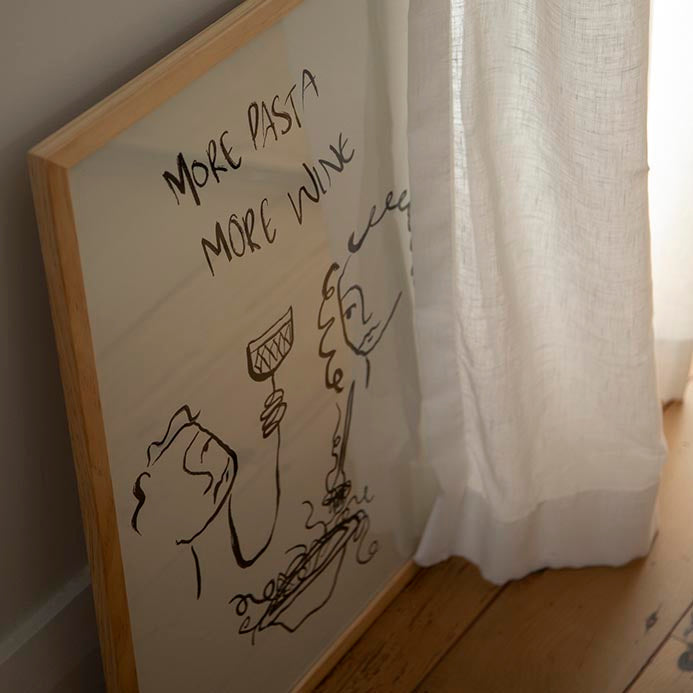 More Pasta More Wine print in a natural frame leaning by a sheer linen curtain