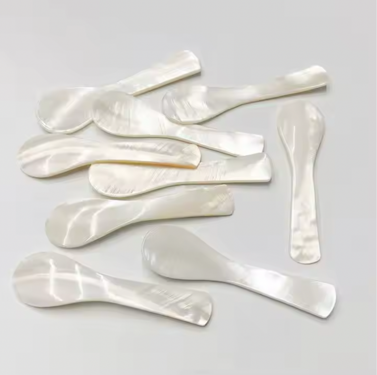Mother of pearl spoons scattered on a pale grey surface