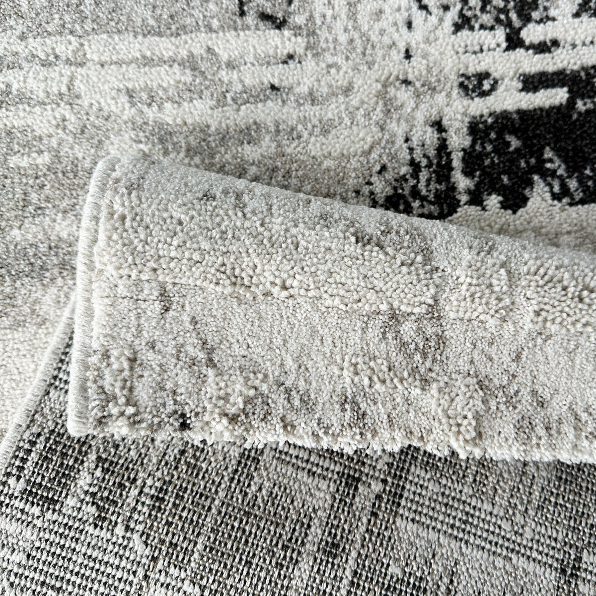 Grey and black rug folded over to show its woven backing