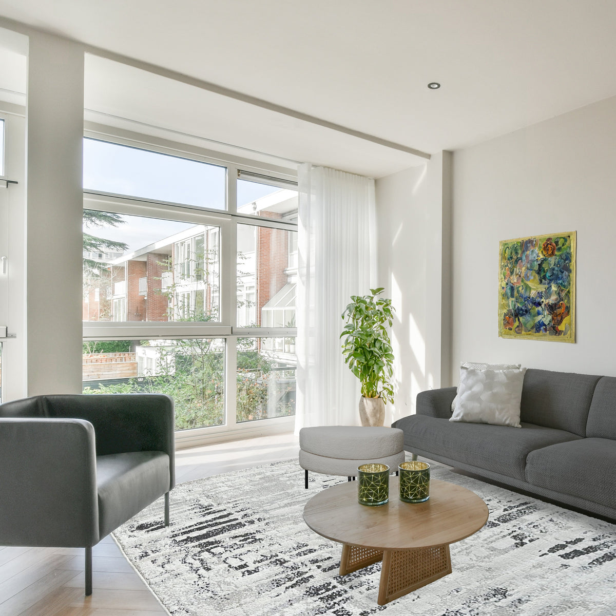 Grey and black abstract rug under a round timber coffee table with a grey sofa and tall windows