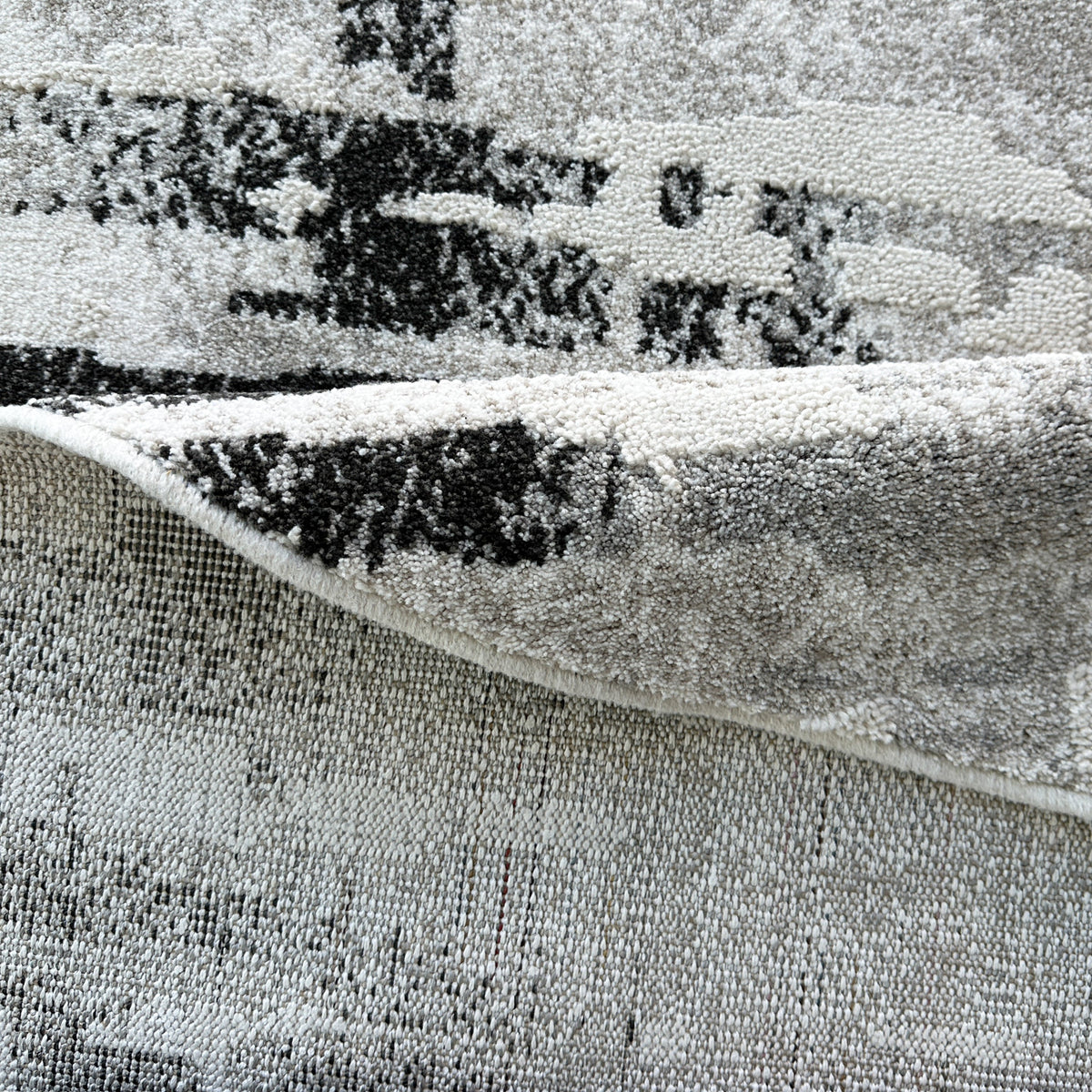 Edge of a round version of the grey and black rug folded to show the backing