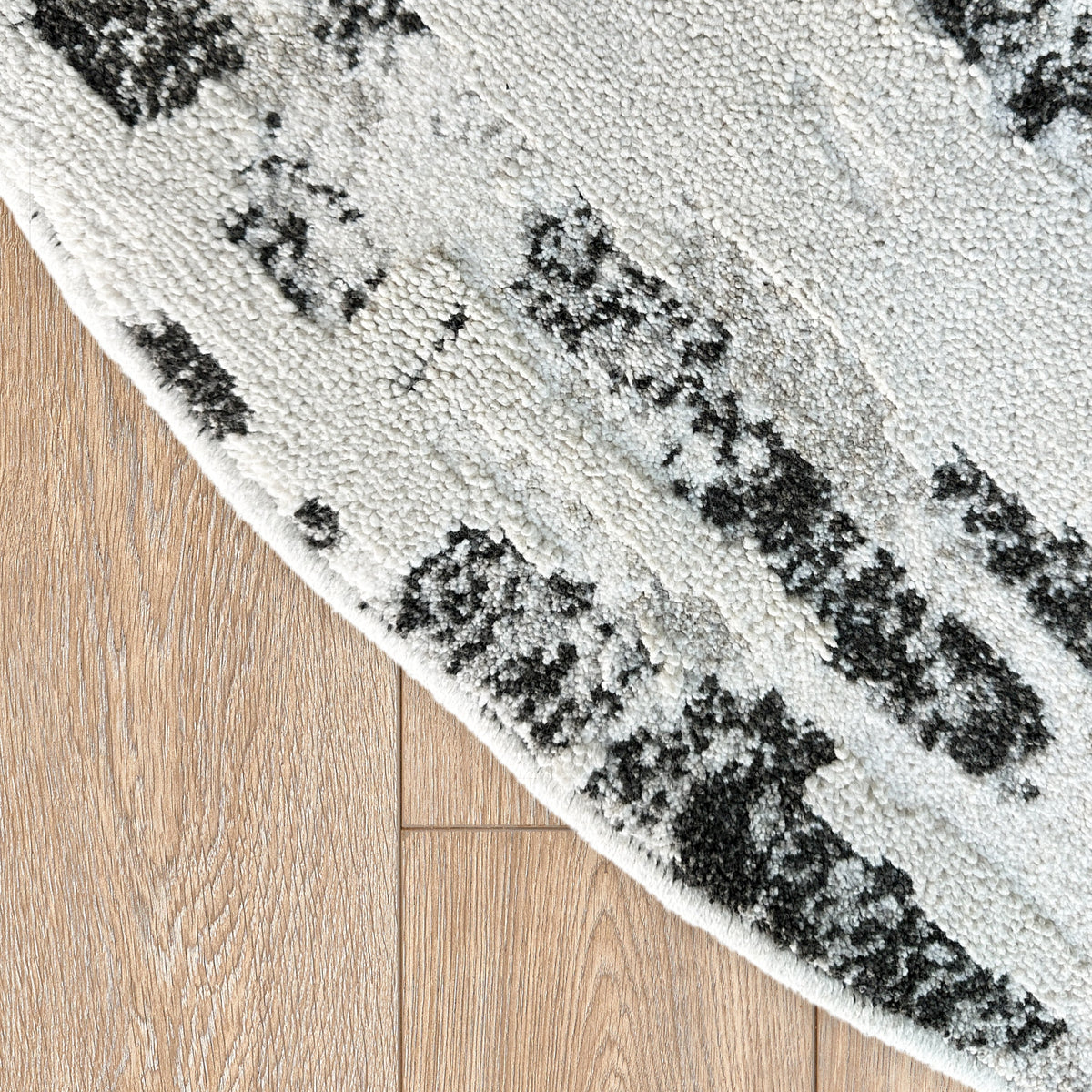 Curved edge of a round version of the grey and black rug on a timber floor