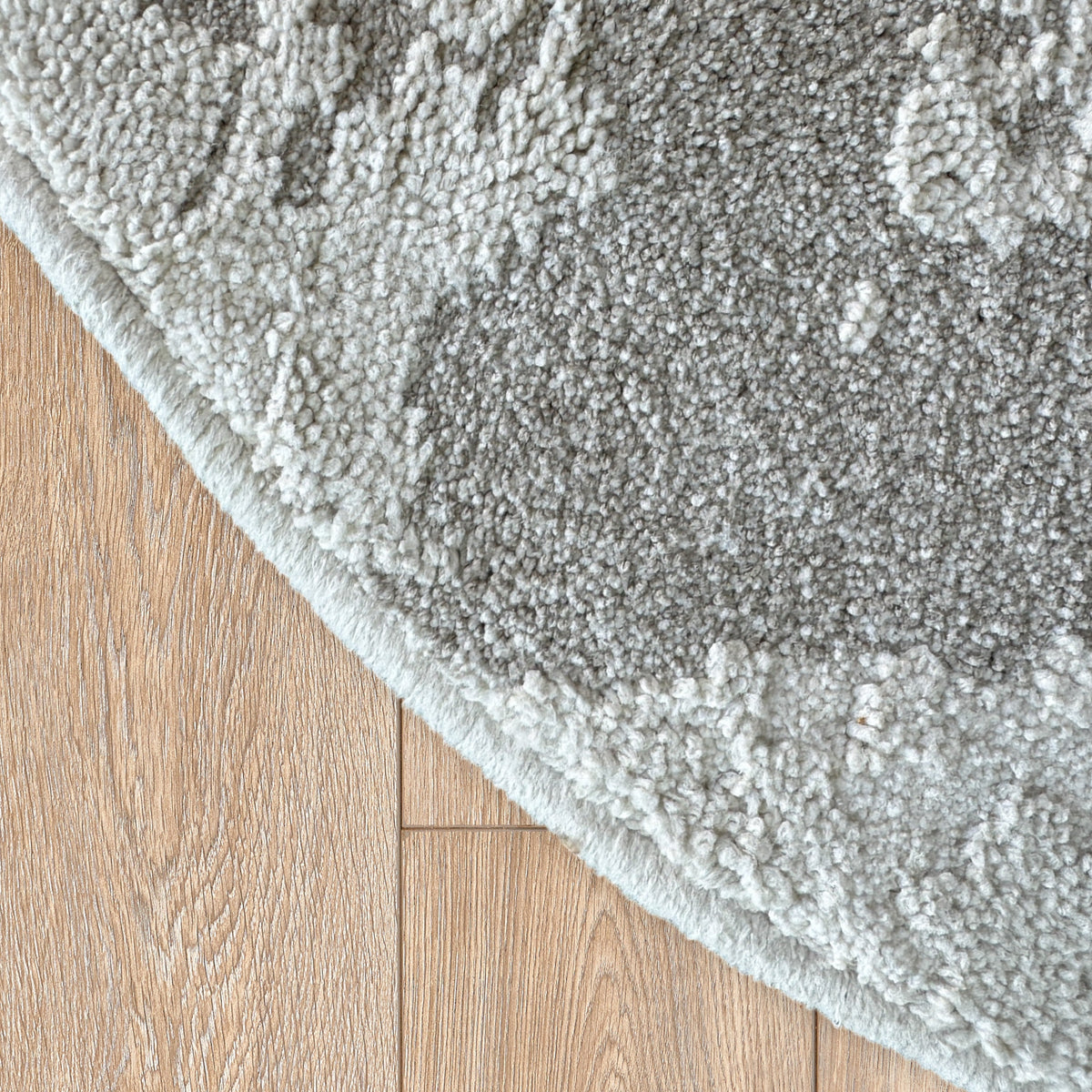 Curved edge of the round grey and beige rug on a timber floor