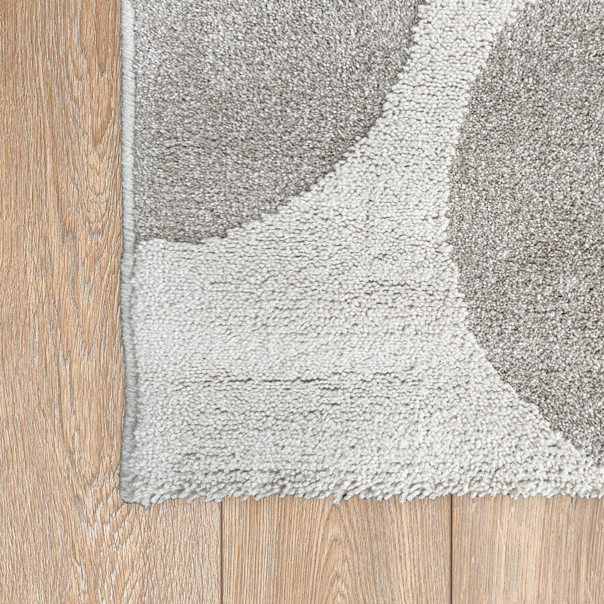 Corner of the beige geometric rug on a light timber floor