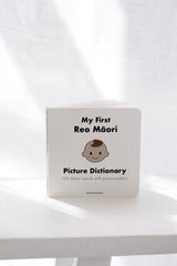 My First Reo Māori Picture Dictionary – 100 Māori words for kids with illustrations and pronunciation, board book for preschoolers on a white surface with a white curtain background.