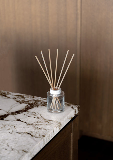 Naturals reed diffuser on the corner of a veined marble bench in front of dark timber panelling