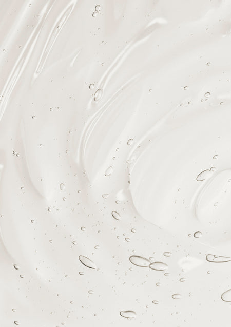 Close-up texture of clear creamy hand and body wash with tiny air bubbles, swirled on a soft white background.
